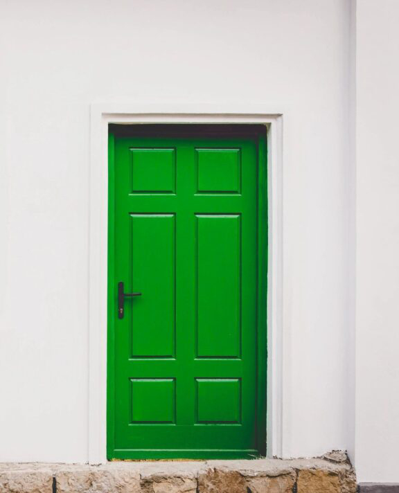 A green door in the corner of a white room.